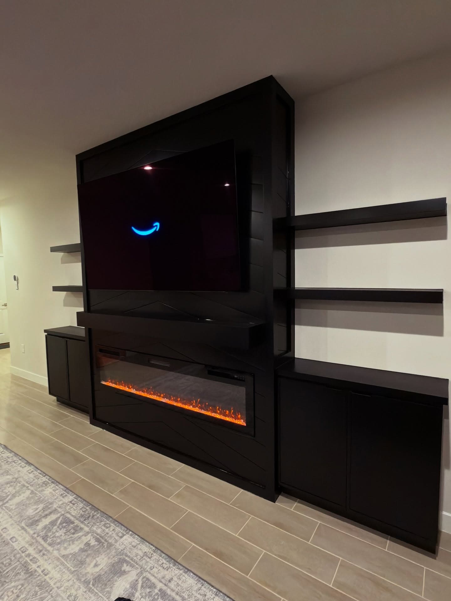 Statement black media wall with extra-wide electric fireplace and floating shelves by AVP Construction JAX